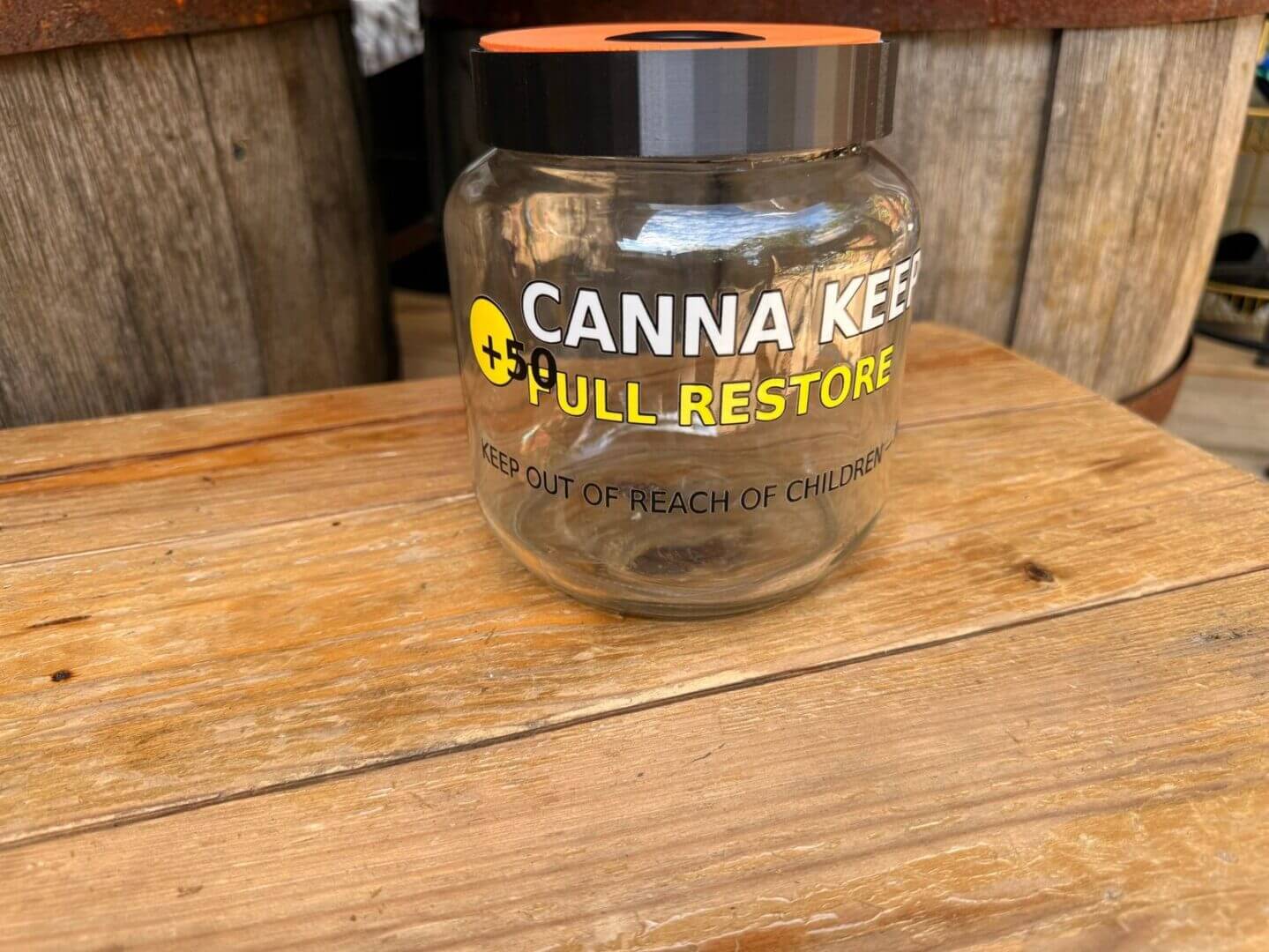 Empty glass jar labeled 'CANNA KEEPER FULL RESTORE' on wooden surface.