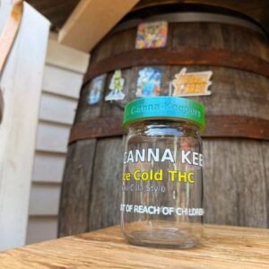 A hand holding a small jar of Anna Kear's Gold Face Serum in front of a wooden barrel.