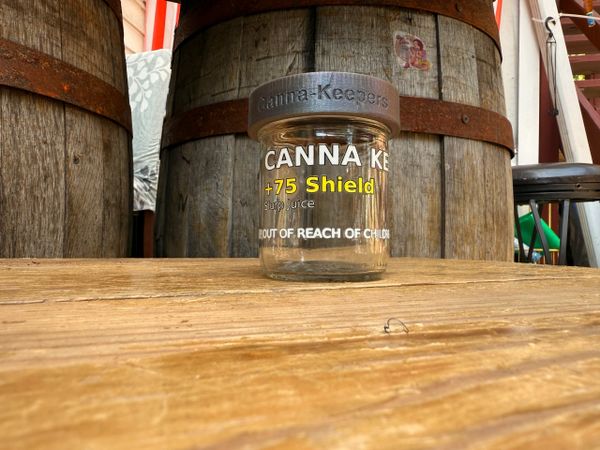 A cannabis product container with barrels in the background.