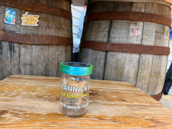 A container of black pepper on a wooden table with barrels in the background.