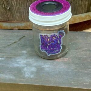 A small glass jar with a purple lid and a purple sticker on a wooden surface.