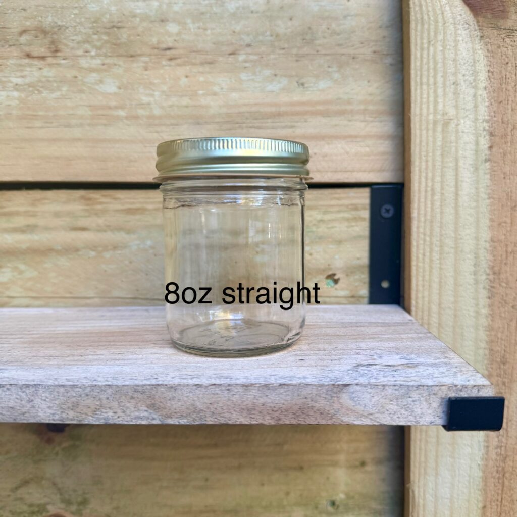 An 8oz straight glass jar with a metal lid on a wooden shelf.