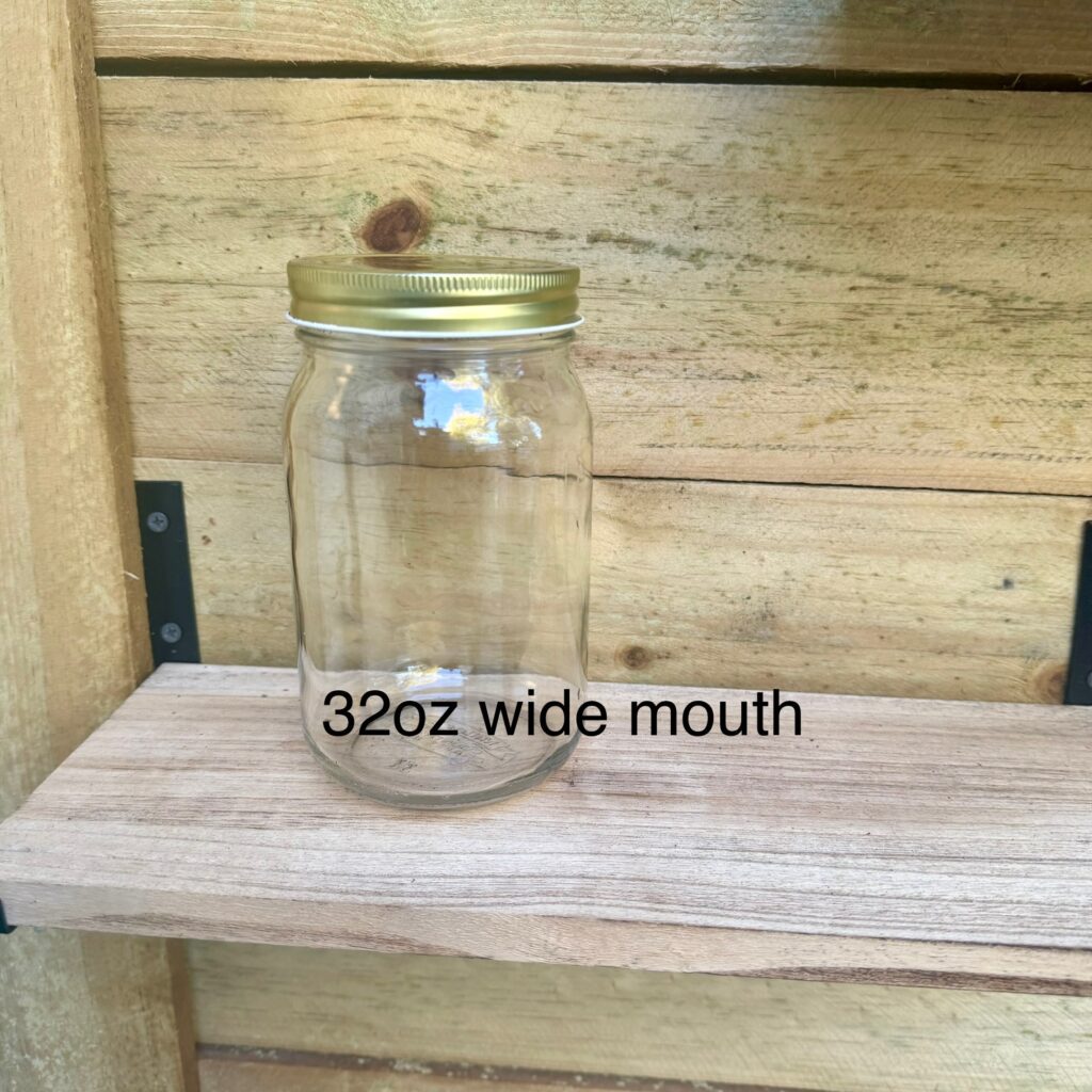 A 32oz wide mouth glass jar with a metal lid on a wooden shelf.