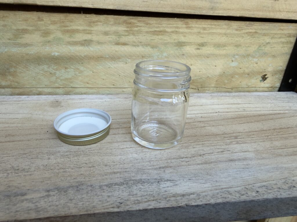Empty glass jar with white lid on wooden surface.