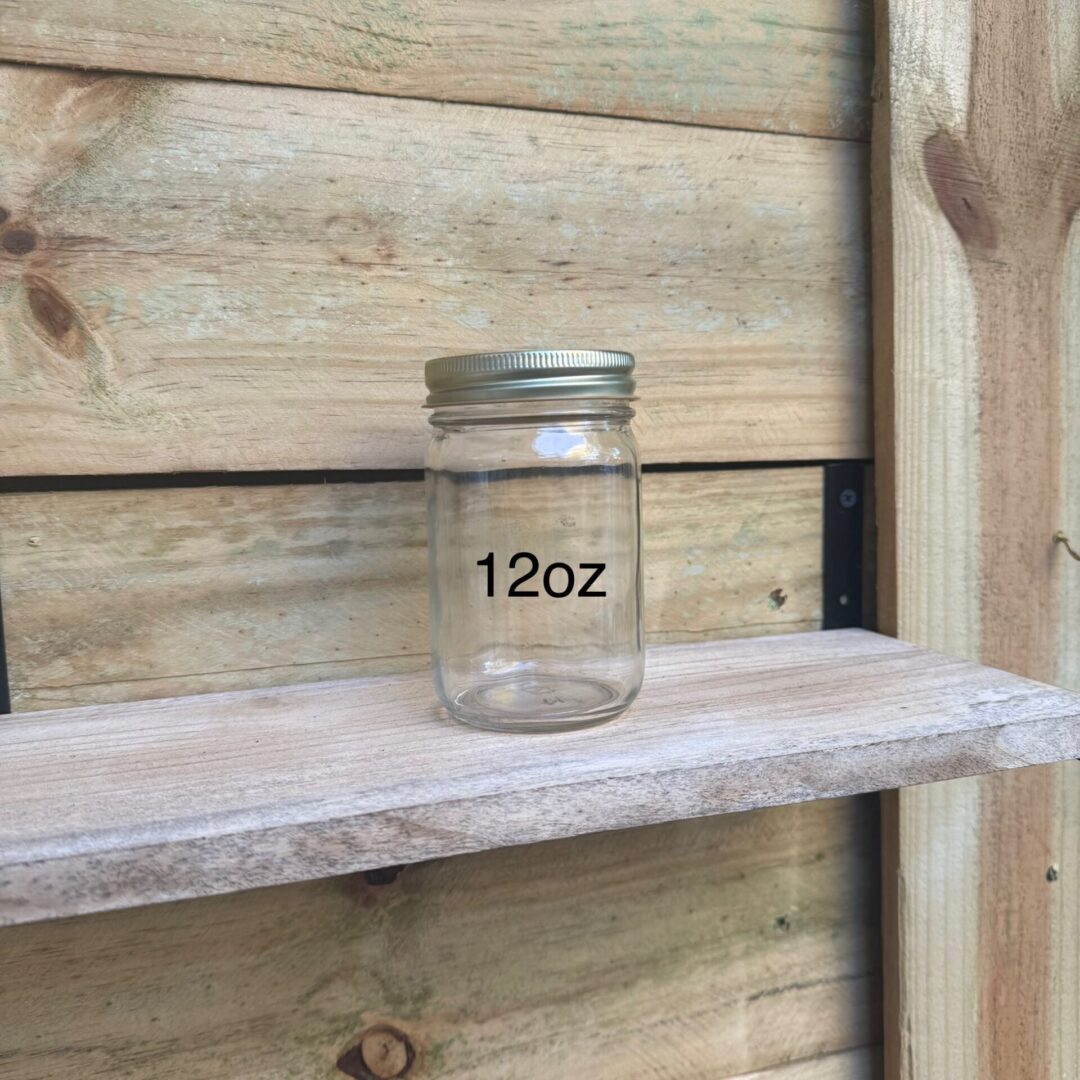 A 12oz clear glass jar on a wooden shelf against a wooden wall.