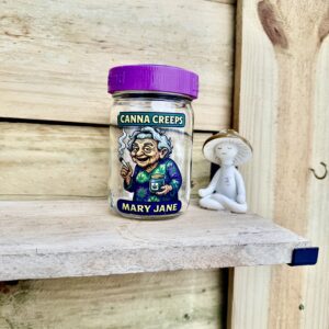 Glass jar "Canna Creeps Mary Jane" beside figurine